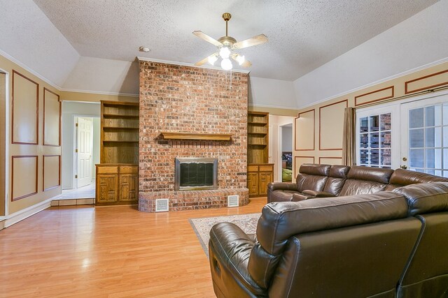 living room featuring lofted ceiling, a brick fireplace, light wood-type flooring, a textured ceiling, and built in features