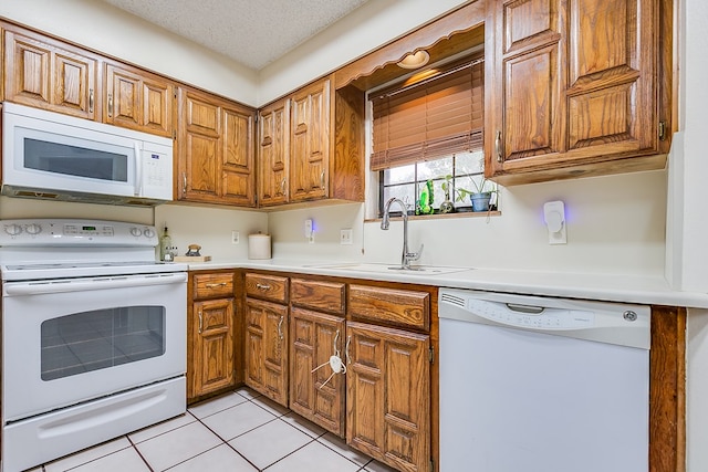 kitchen featuring sink, white appliances, light tile patterned floors, and a textured ceiling