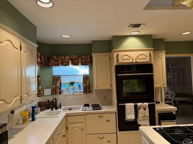 kitchen featuring black double oven, tile countertops, sink, and backsplash