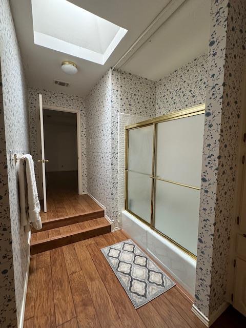 bathroom featuring wood-type flooring, shower / bath combination with glass door, and a skylight