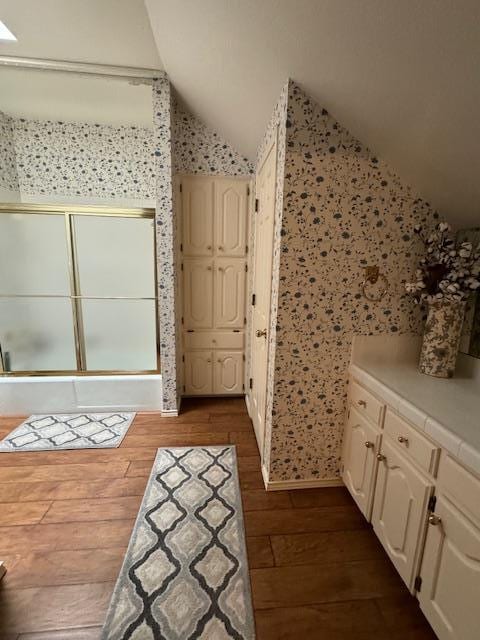 bathroom with a shower with door, wood-type flooring, and vaulted ceiling