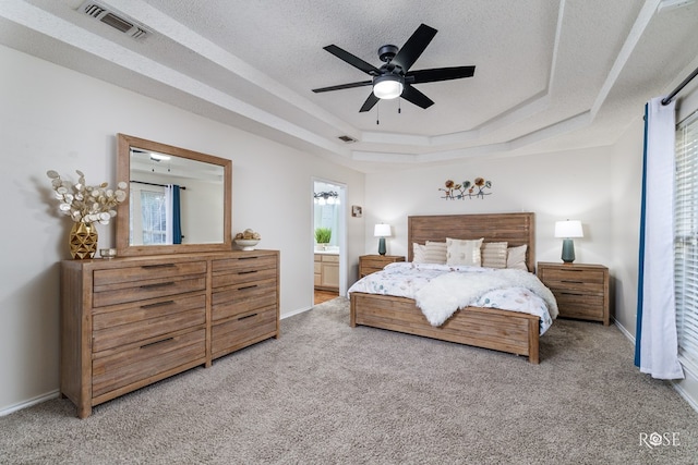 carpeted bedroom with ensuite bathroom, a textured ceiling, ceiling fan, and a tray ceiling