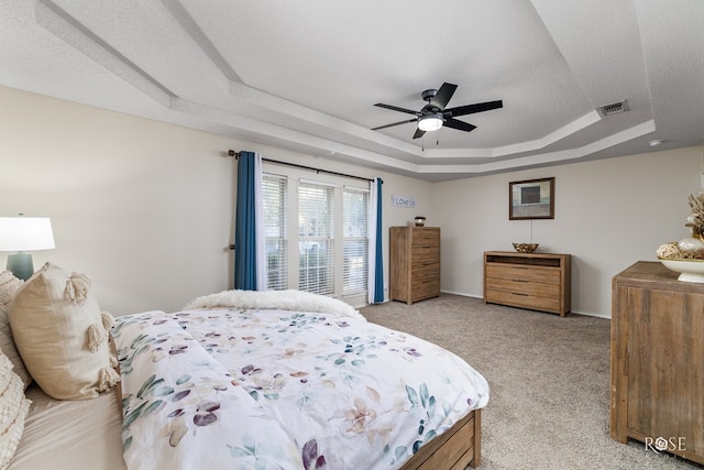 bedroom with ceiling fan, a raised ceiling, light carpet, and a textured ceiling