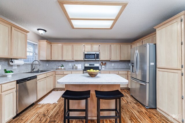 kitchen featuring sink, appliances with stainless steel finishes, light hardwood / wood-style floors, a kitchen island, and light brown cabinets