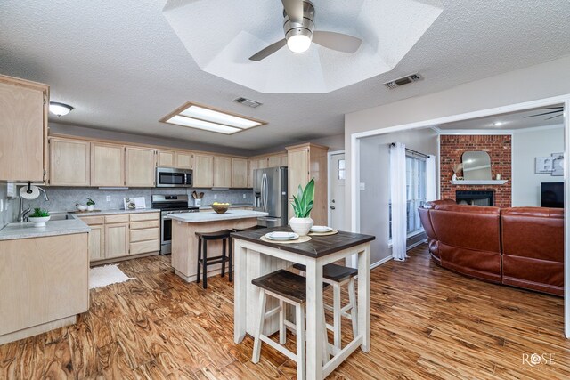 kitchen with a breakfast bar, appliances with stainless steel finishes, tasteful backsplash, a kitchen island, and light brown cabinetry