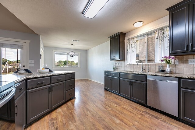 kitchen with sink, hanging light fixtures, light wood-type flooring, stainless steel dishwasher, and backsplash