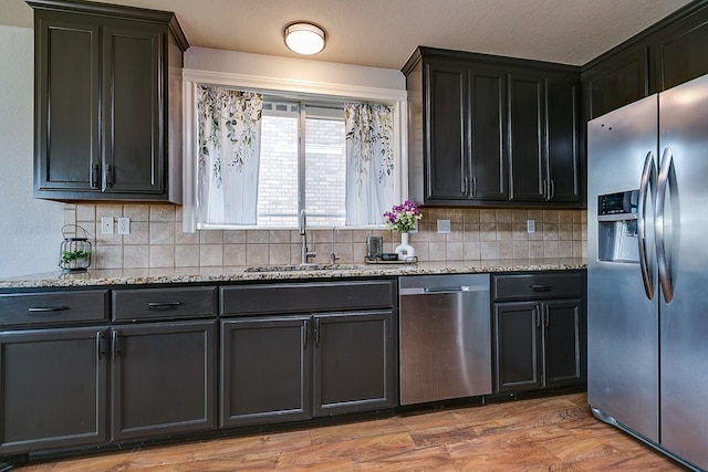 kitchen with sink, backsplash, stainless steel appliances, light stone counters, and light wood-type flooring