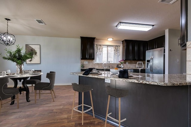 kitchen featuring decorative light fixtures, dark hardwood / wood-style flooring, decorative backsplash, stainless steel fridge with ice dispenser, and light stone countertops