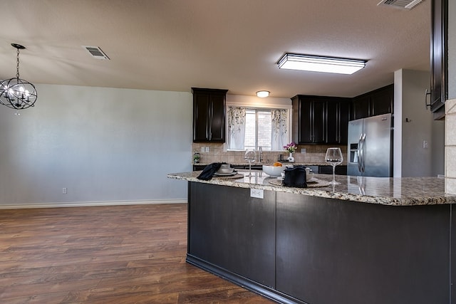 kitchen with tasteful backsplash, dark hardwood / wood-style flooring, hanging light fixtures, stainless steel fridge with ice dispenser, and light stone countertops