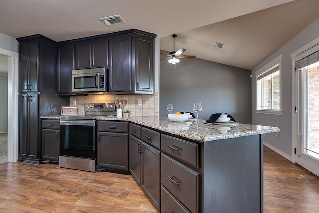 kitchen with appliances with stainless steel finishes, light stone counters, wood-type flooring, vaulted ceiling, and kitchen peninsula