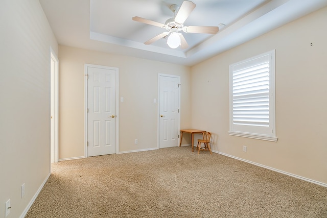 carpeted spare room with a tray ceiling and ceiling fan