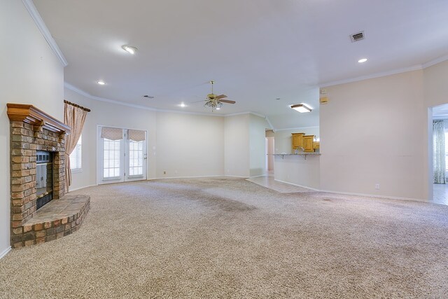 unfurnished living room with a brick fireplace, crown molding, carpet floors, and ceiling fan