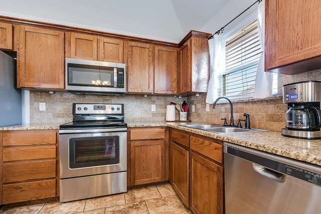 kitchen featuring tasteful backsplash, sink, light stone counters, and appliances with stainless steel finishes