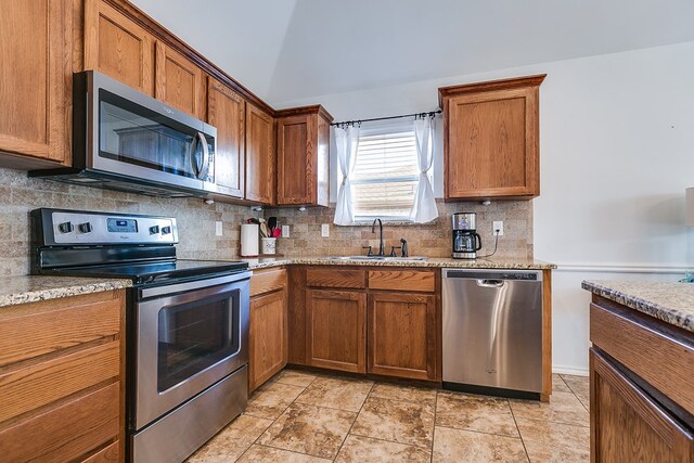 kitchen with lofted ceiling, sink, stainless steel appliances, light stone countertops, and decorative backsplash