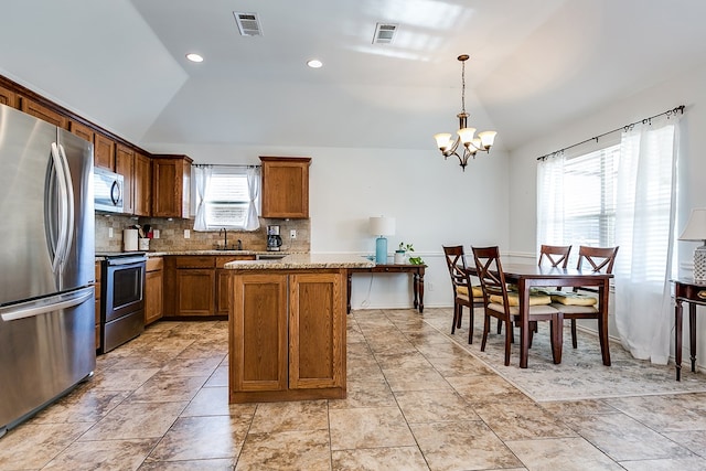 kitchen featuring light stone counters, decorative light fixtures, vaulted ceiling, and appliances with stainless steel finishes