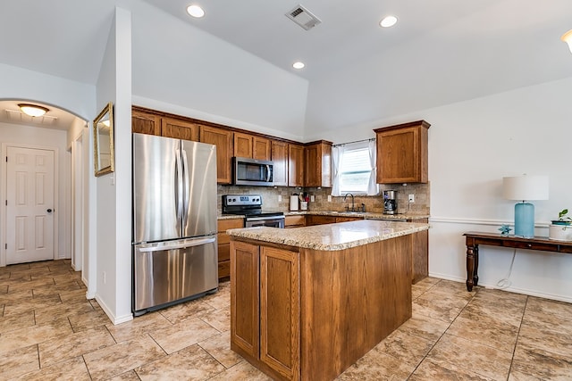 kitchen featuring vaulted ceiling, appliances with stainless steel finishes, tasteful backsplash, a center island, and light stone countertops