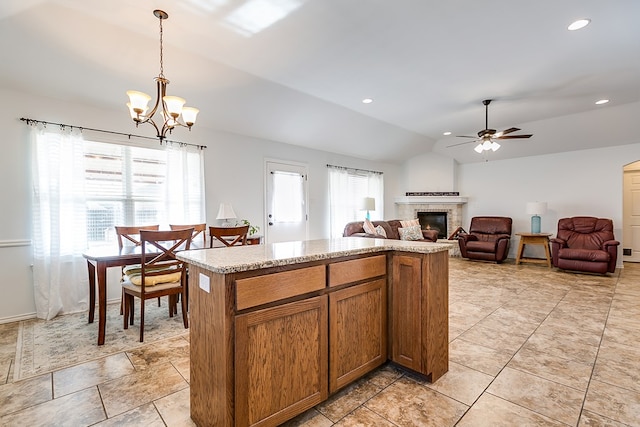 kitchen with lofted ceiling, a stone fireplace, a kitchen island, pendant lighting, and ceiling fan with notable chandelier