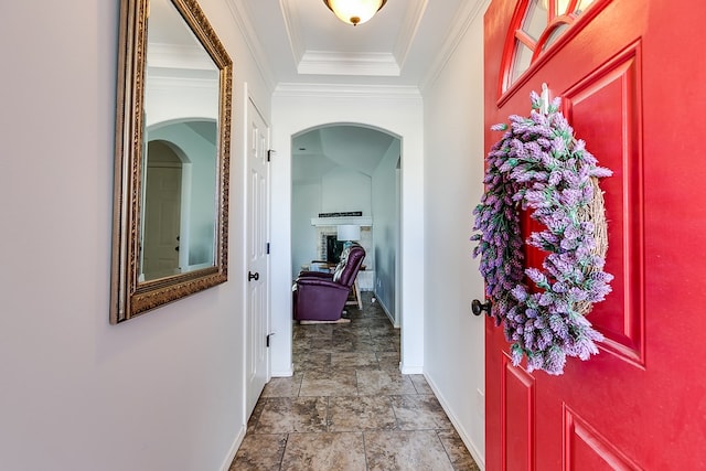 foyer entrance featuring a raised ceiling, crown molding, and a brick fireplace