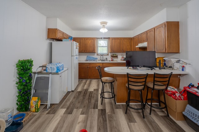 kitchen with white refrigerator, kitchen peninsula, a breakfast bar area, and light wood-type flooring