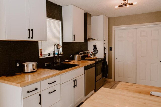 kitchen with wall chimney exhaust hood, butcher block counters, sink, white cabinetry, and appliances with stainless steel finishes