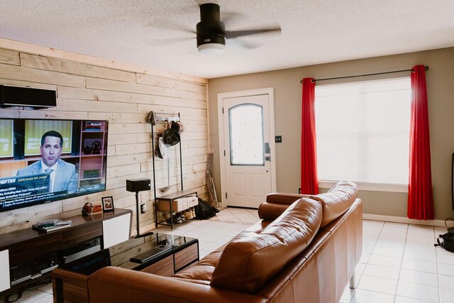 tiled living room featuring ceiling fan, a textured ceiling, and wood walls