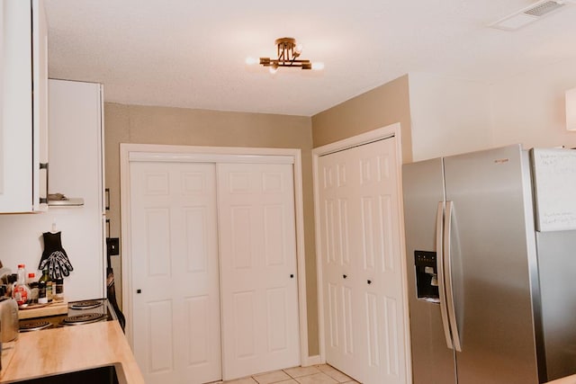 kitchen with light tile patterned floors, white cabinets, and stainless steel fridge with ice dispenser