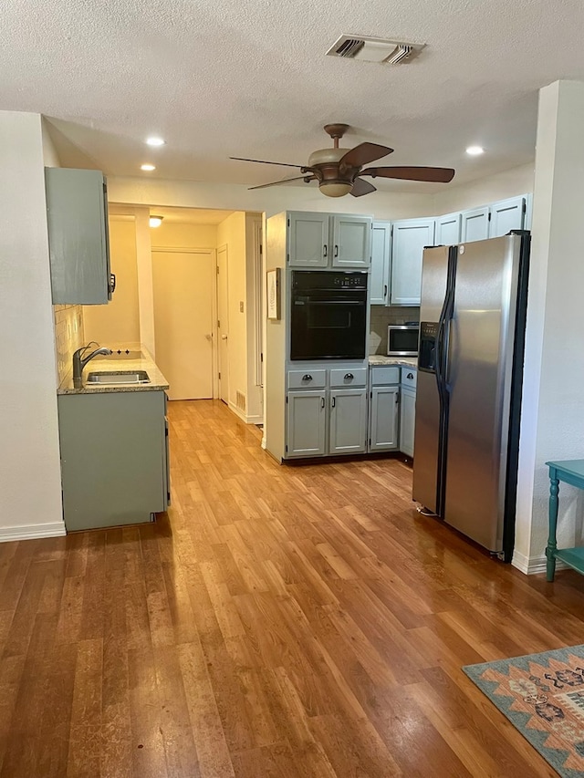 kitchen with sink, light hardwood / wood-style flooring, ceiling fan, stainless steel appliances, and a textured ceiling