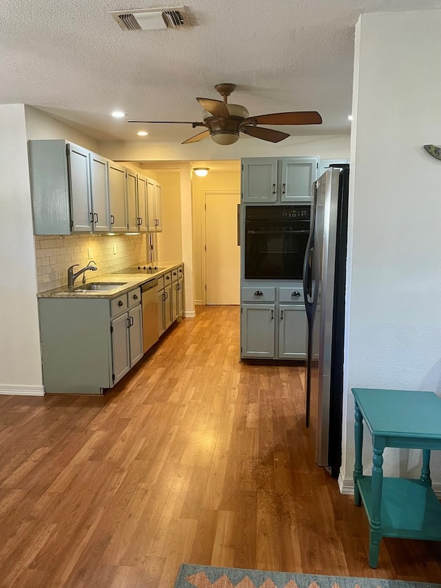 kitchen with sink, appliances with stainless steel finishes, tasteful backsplash, a textured ceiling, and light wood-type flooring