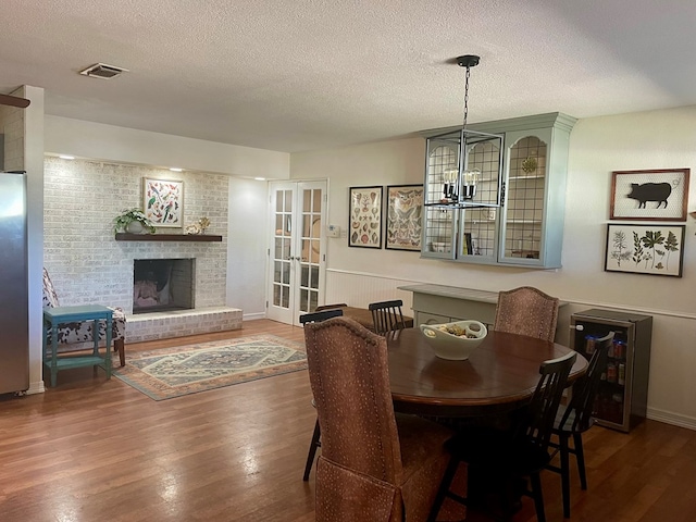 dining room featuring an inviting chandelier, a fireplace, a textured ceiling, dark hardwood / wood-style flooring, and french doors