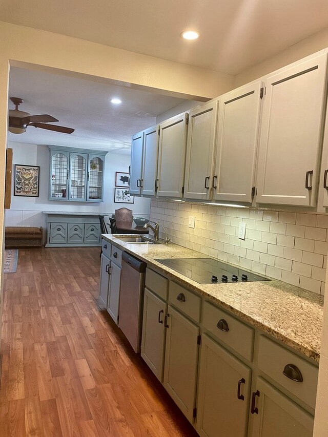 kitchen featuring tasteful backsplash, dishwasher, black electric stovetop, light hardwood / wood-style floors, and light stone countertops