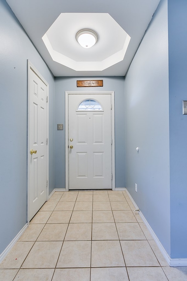 doorway with a tray ceiling, baseboards, and light tile patterned flooring