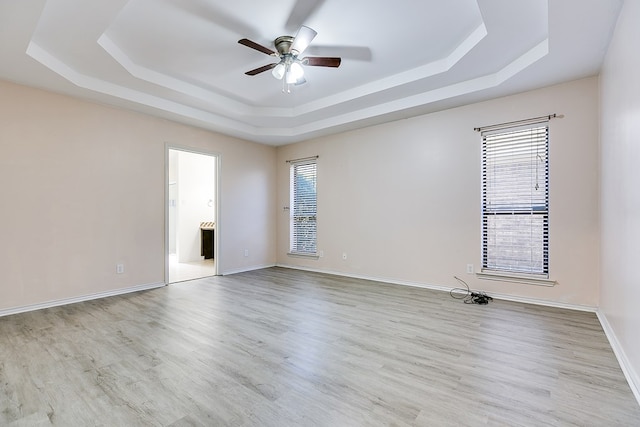 spare room with a tray ceiling, baseboards, wood finished floors, and a ceiling fan