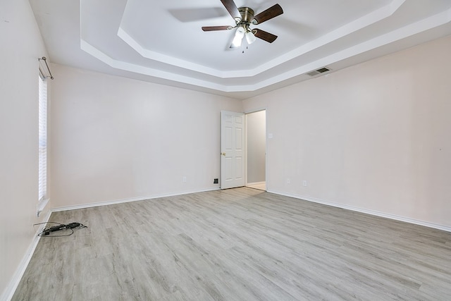 empty room featuring visible vents, baseboards, a tray ceiling, wood finished floors, and a ceiling fan