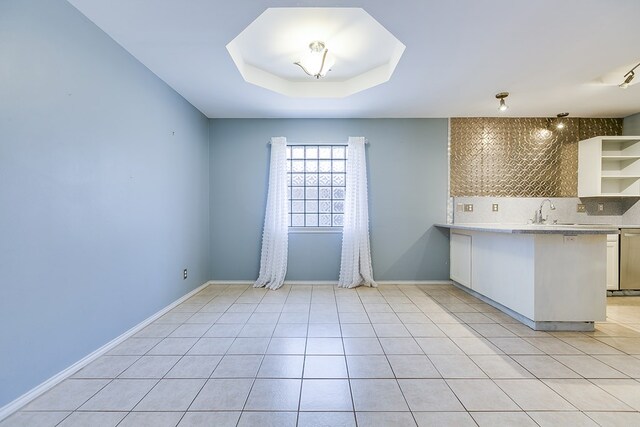 kitchen featuring open shelves, a sink, backsplash, light countertops, and a raised ceiling