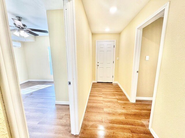 hallway with an AC wall unit and light hardwood / wood-style flooring