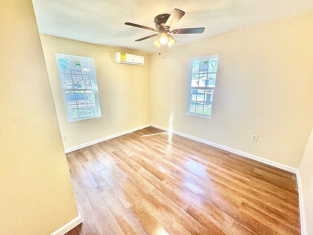 spare room featuring an AC wall unit, a wealth of natural light, ceiling fan, and light hardwood / wood-style flooring