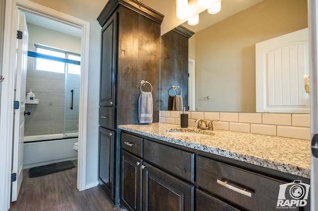 bathroom featuring toilet, shower / bath combination with glass door, wood finished floors, vanity, and decorative backsplash