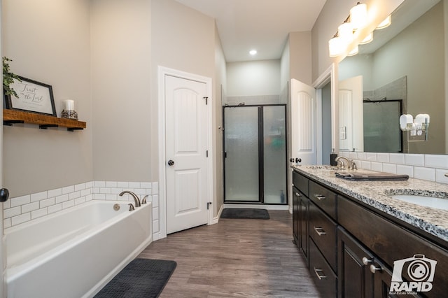 bathroom featuring double vanity, a shower stall, a sink, and wood finished floors