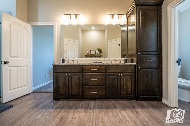 full bathroom featuring toilet, wood finished floors, a sink, baseboards, and double vanity