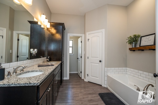 bathroom with double vanity, a garden tub, a sink, and wood finished floors