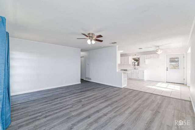 unfurnished living room with sink, ceiling fan, and light wood-type flooring