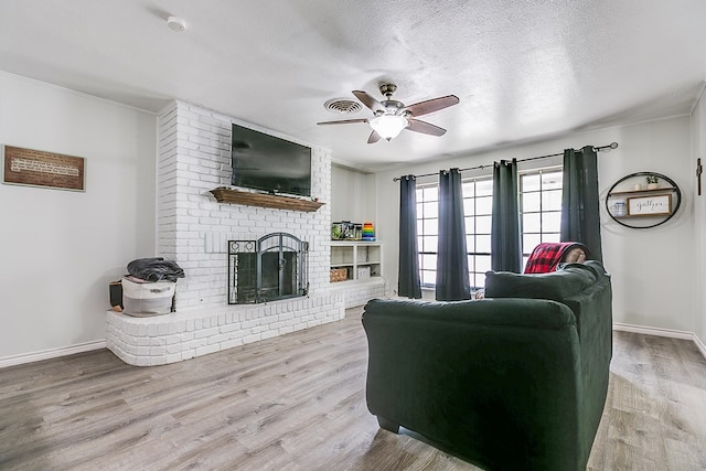 living room with ceiling fan, a fireplace, a textured ceiling, and light wood-type flooring