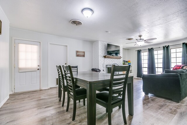 dining area featuring ceiling fan, a brick fireplace, a textured ceiling, and light hardwood / wood-style floors