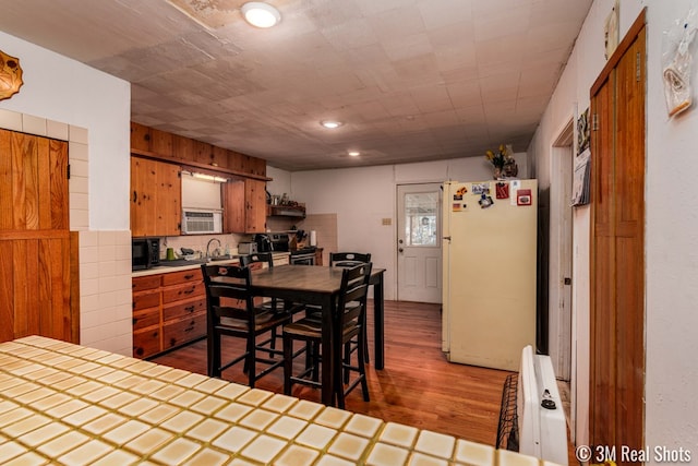 kitchen with brown cabinetry, tile countertops, freestanding refrigerator, stainless steel range with electric stovetop, and black microwave