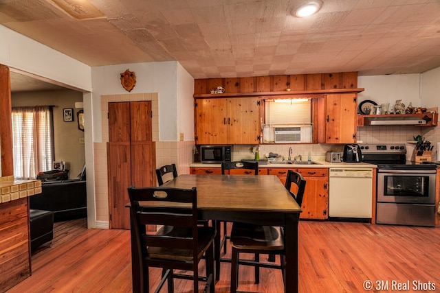 kitchen with light wood finished floors, electric stove, dishwasher, a sink, and exhaust hood