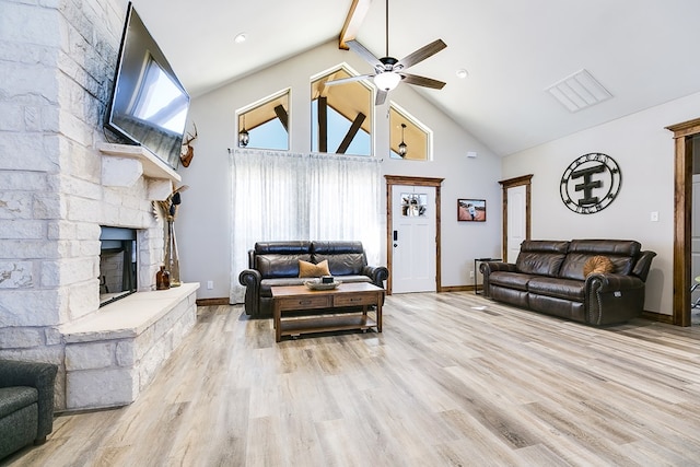 living room with ceiling fan, a stone fireplace, beam ceiling, high vaulted ceiling, and light wood finished floors