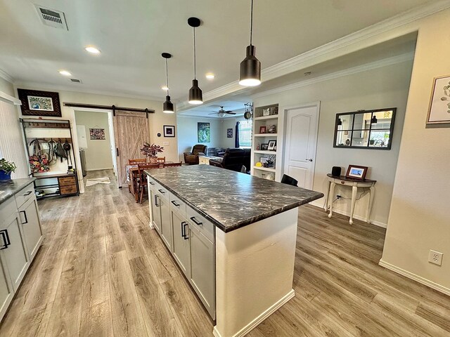7754 S Copper Mountain Cir, San Angelo, TX 76901 - kitchen with a barn door, crown molding, light wood-style floors, white cabinets, and hanging light fixtures