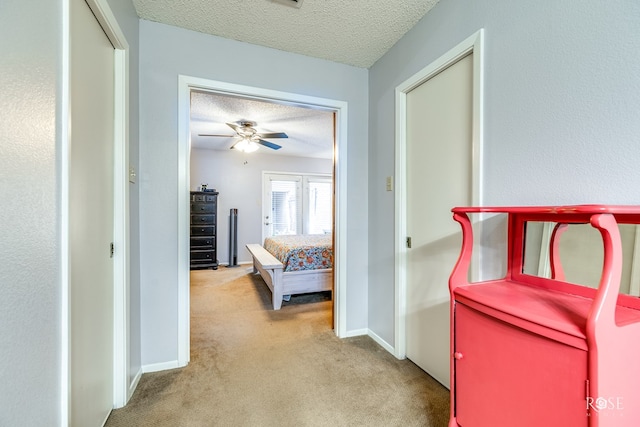 hall featuring baseboards, a textured ceiling, and light colored carpet