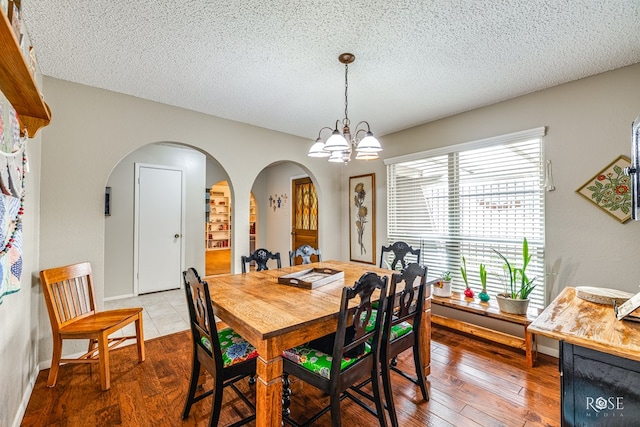 dining room featuring wood-type flooring, a textured ceiling, arched walkways, and a notable chandelier