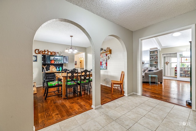 dining room with an inviting chandelier, built in shelves, a textured ceiling, and tile patterned floors